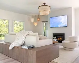 sala de estar luminosa en una paleta de colores blancos y naturales, cuatro luces colgantes texturizadas, un gran sofá color crema y un sofá de madera oscura, una alfombra color crema y un sillón