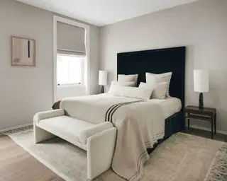 Nøytralt moderne soverom, gråmalte vegger, mørkt tregulv med teppe, stor seng med svart polstret hodegjerde, krem sengetøy og puter, bucle-polstret daybed ved fotenden av sengen