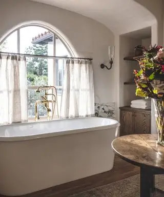 salle de bains blanche avec baignoire autoportante et fenêtre cintrée