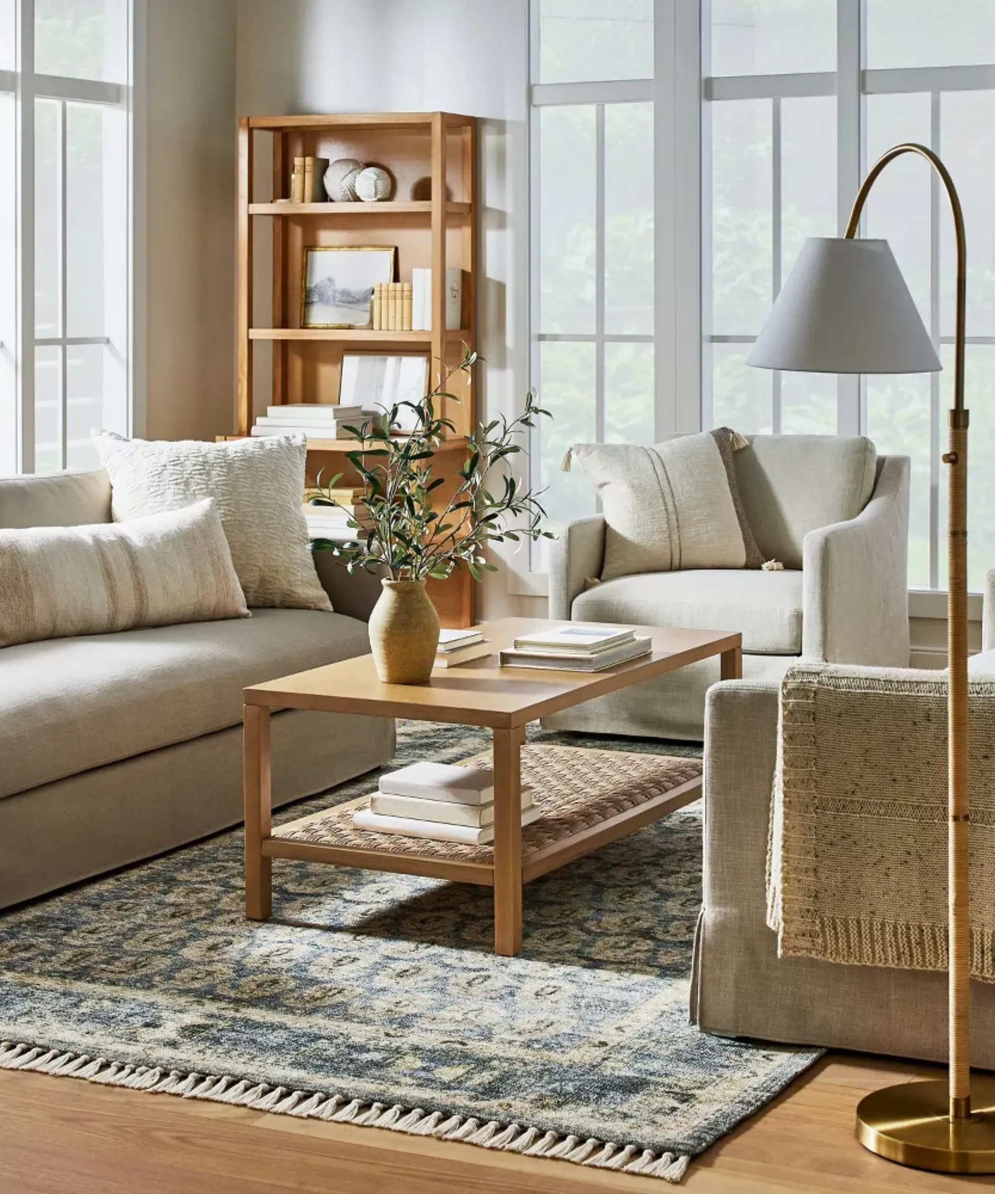 en stue med en beige sofa en beige accentstol et rektangulært sofabord i træ med en blomstervase på toppen og et blåt persisk-inspireret tæppe på gulvet' loading='lazy' title=