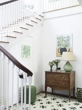ingresso bianco con opere illustrative, cassettiera, tappeto verde e crema, lampada
