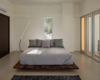 Quarto brutalista com piso de concreto, cama com plataforma de madeira, guarda-roupas e portas de pátio