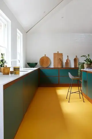 Cocina con gabinetes de color verde azulado con piso de color amarillo brillante y tablas de cortar de madera.