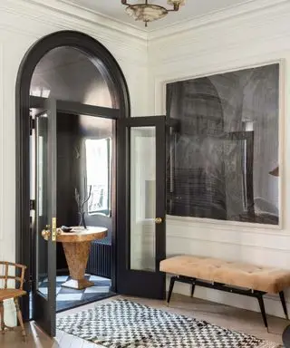 Couloirs beiges avec porte cintrée noire et tapis en damier