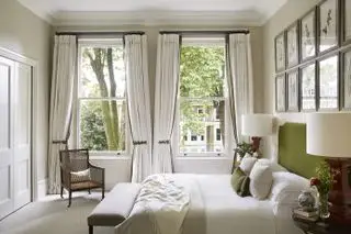 Dormitorio blanco/crema con cabecera verde, paredes empapeladas en color crema, obras de arte y cortinas dobles