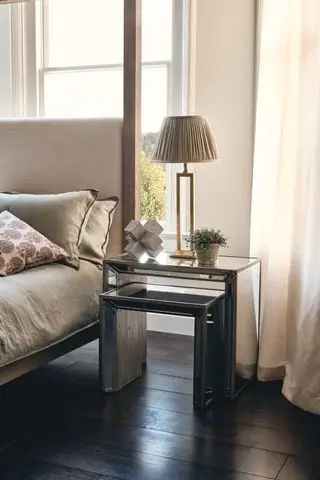esquema de dormitorio neutro con cabecera tapizada, piso de madera oscura y mesas auxiliares de vidrio veneciano