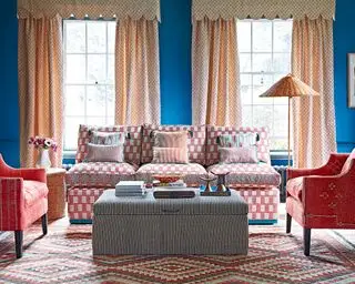 Ideias para cortinas de janela grande com cortinas estampadas bege com saia, em uma sala de estar azul com poltronas e sofá vermelhos