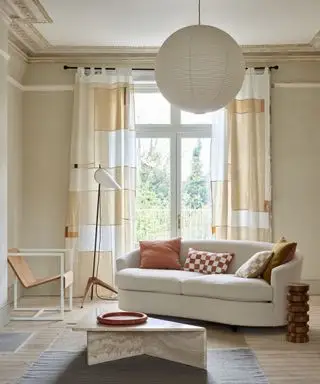 Moderne kremstue med abstrakte trykte gardiner, buet sofa, teppe, salongbord, lanterneanheng