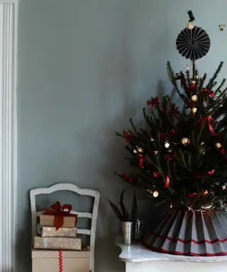 Pequeño árbol de Navidad con adornos rojos y dorados y falda gris.