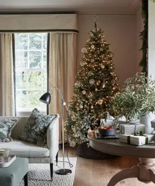 Árbol de Navidad clásico en salón moderno con luces blancas.