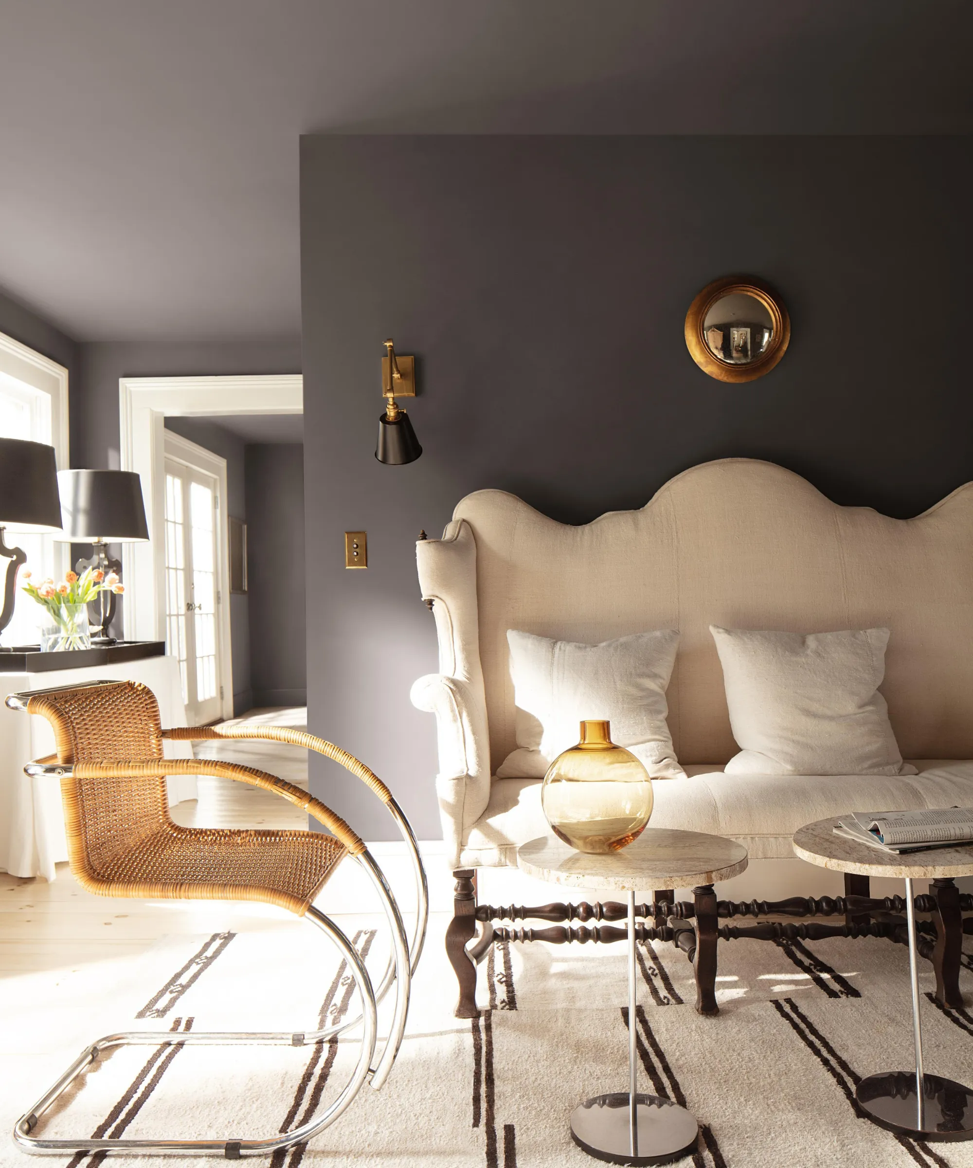 un salon avec un grand canapé blanc, une chaise d'appoint en rotin, deux tables à boissons et des murs et un plafond peints avec la silhouette de Benjamin Moore.' loading='lazy' title=