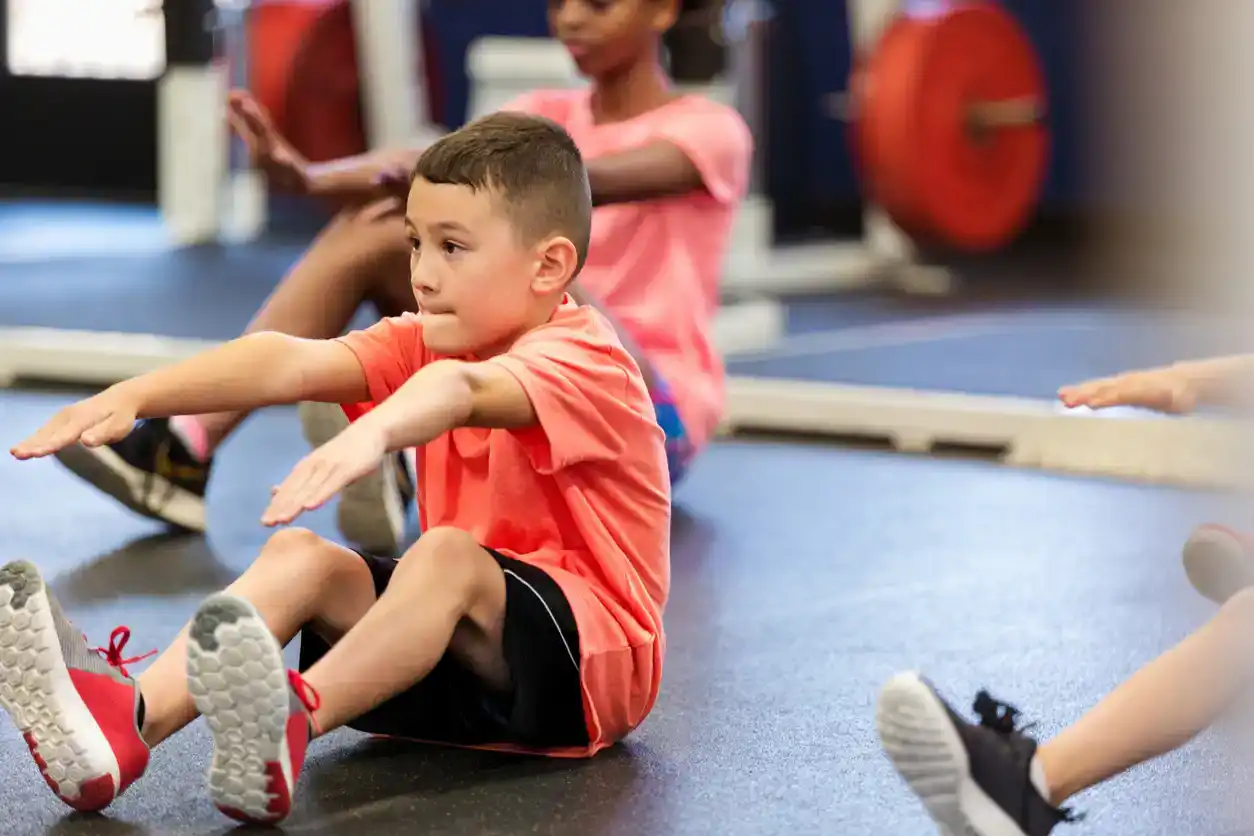 Elementary schoolboy concentrates while performing a sit up during fitness class or PE class.