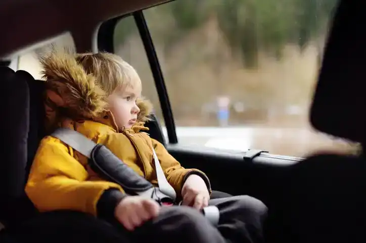 Portrait of little boy sitting in car seat during roadtrip or travel.
