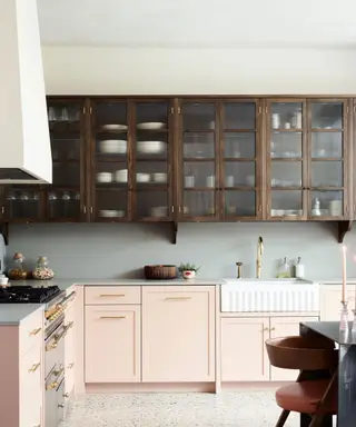 Uma cozinha com armários inferiores rosa e armários superiores de madeira com frentes de vidro