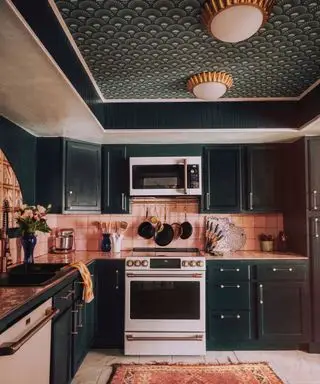 Køkken med mørkegrøn og guld art deco inspireret tapet, matchende mørkegrønne skabe, lyserøde vægfliser, marmorgulve, lyserødt mønstret tæppe