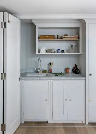 Une porte pliante blanche séparant une buanderie entièrement blanche avec des comptoirs en marbre gris et des étagères ouvertes.