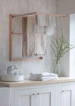 Idées de petites buanderies comprenant un séchoir en bois dépliable dans un décor blanc et neutre avec un grand vase de fleurs.