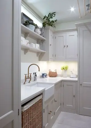 Armoires gris pâle installées dans une petite buanderie en forme de L, avec comptoir et carrelage blancs.