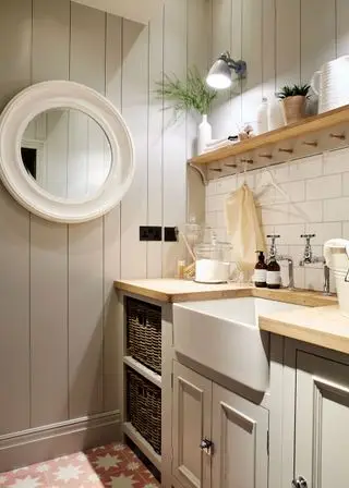 Une buanderie gris pâle lambrissée de bois avec un évier de majordome, des carreaux de métro blancs, des comptoirs en bois et une étagère ouverte.