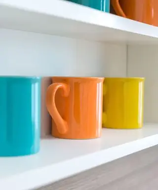 Una taza de café azul, naranja y amarilla alineada sobre un estante blanco