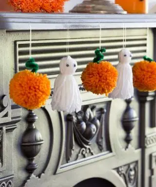 Řemeslné projekty pro Halloween. Oranžové ručně vyráběné pom-pom dýně a střapec duchové visící na plášti.