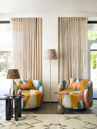 sala de estar con sillones a juego con tela con estampado llamativo, alfombra estampada, mesa auxiliar negra, cortinas, lámpara de pie con pantalla estampada, lámpara de mesa con pantalla estampada