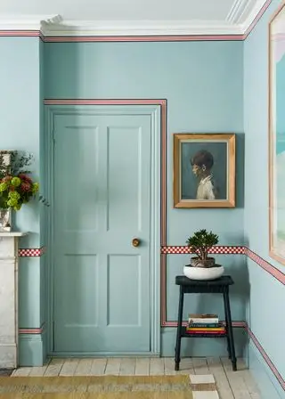 salón azul con borde rojo, taburete negro con planta, obras de arte, marco de fuego, suelo de madera y alfombra.