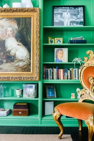 salón con librería pintada de verde brillante, silla vintage tapizada en terciopelo, pintura vintage con marco dorado adornado
