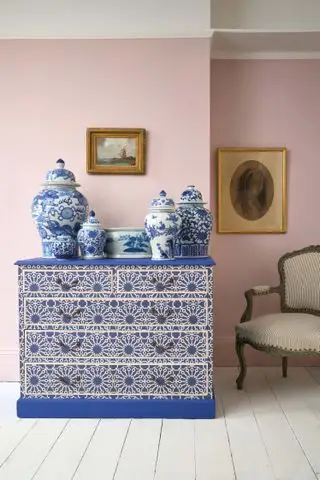 salón rosa con cómoda decoupage Annie Sloan, vasijas de cerámica azules y blancas, suelo pintado de blanco, sillón antiguo y cuadros antiguos