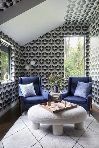 malá herna s grafickou tapetou, dvě modrá křesla, vrhcáby na konferenčním stolku Boucle, retro stojací lampa, černobílá strana s listy, nebílý grafický koberec, podlaha z tvrdého dřeva