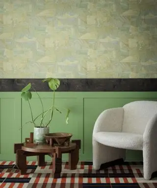 Sala de estar com papel de parede dado atelier em papel de parede Matthew Burrows sterno, painéis pintados de verde, poltrona boucle, mesa de centro em madeira escura, tapete listrado vermelho, creme e preto