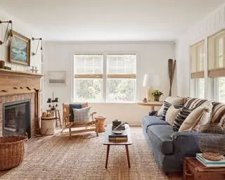 Una idea de sala de estar estrecha con una paleta de colores neutros, alfombra de yute, sofá azul y chimenea de madera.