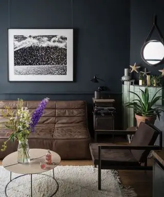 Stue malet en mørkegrå af Farrow & Ball, brun lædersofa, grøn flisebelagt pejs, trægulv med cremet tæppe, hvidmalet loft, sort/hvid kunst på væggen, kysttilbehør og maritimt spejldesign over pejsen