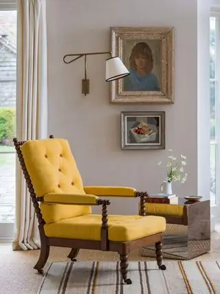 Salón con sillón amarillo, cuadros en la pared, mesita auxiliar y aplique.