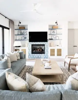 Salón azul y blanco con alcobas para libros, azulejos azules alrededor del fuego y apliques negros