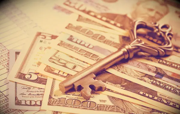 Money on a table with an old key on top of the bills.