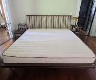 Materasso in lattice organico PlushBeds Botanical Bliss su un letto contro un muro bianco.