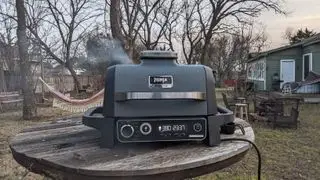 Die Räucherkammer des Ninja Woodfire Außengrills, gefüllt mit Pellets, stand auf einem hölzernen Gartentisch