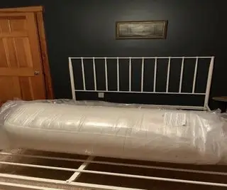 Matelas Birch Luxe Natural enveloppé sur un cadre de lit contre un mur bleu.