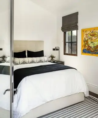 Camera da letto monocromatica con pareti dipinte di bianco, biancheria da letto in bianco e nero, tappeto a righe nere, crema e grigie, opere d'arte in giallo brillante