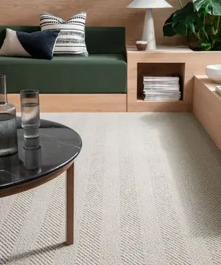 Tapete texturizado creme na sala de estar moderna, construído em assentos de madeira com almofadas verdes, mesa de centro redonda preta, plantas e livros