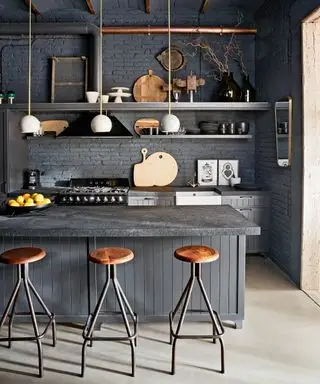 Un ejemplo de ideas de estanterías de cocina que muestra una cocina gris con una isla y taburetes de bar de madera de estilo industrial.