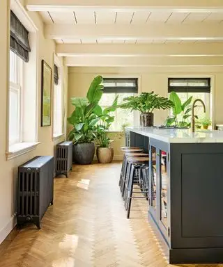 cuisine neutre avec îlot gris foncé, parquet à chevrons, tabourets de bar en bois et radiateurs gris foncé
