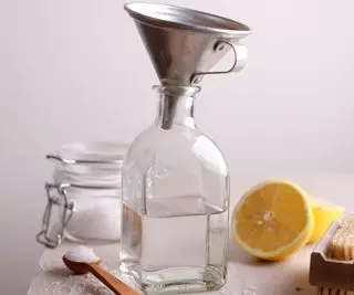 Una bottiglia di vetro con un imbuto di acciaio inossidabile all'interno e attorno una fetta di limone e un cucchiaino di bicarbonato di sodio