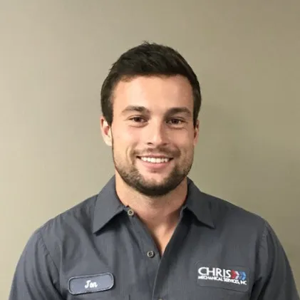 Jon est un homme aux cheveux bruns et une barbe courte portant une chemise de travail à col gris avec le nom de l'entreprise et son nom cousu.' loading='lazy' title=