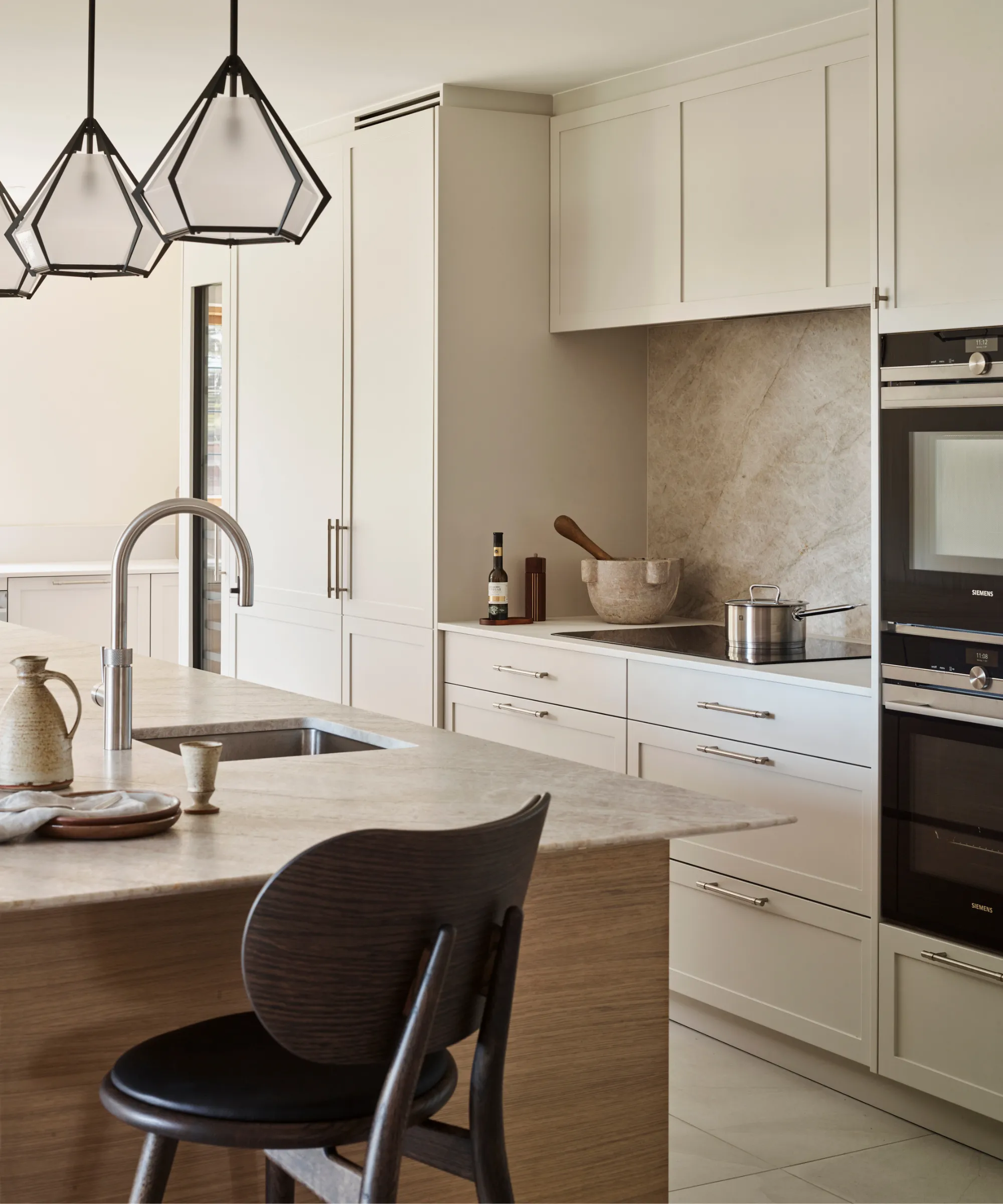 cozinha moderna e minimalista com armários e balcões brancos. backsplash de pedra natural atrás do fogão de vidro e uma ilha de pedra correspondente' loading='lazy' title=