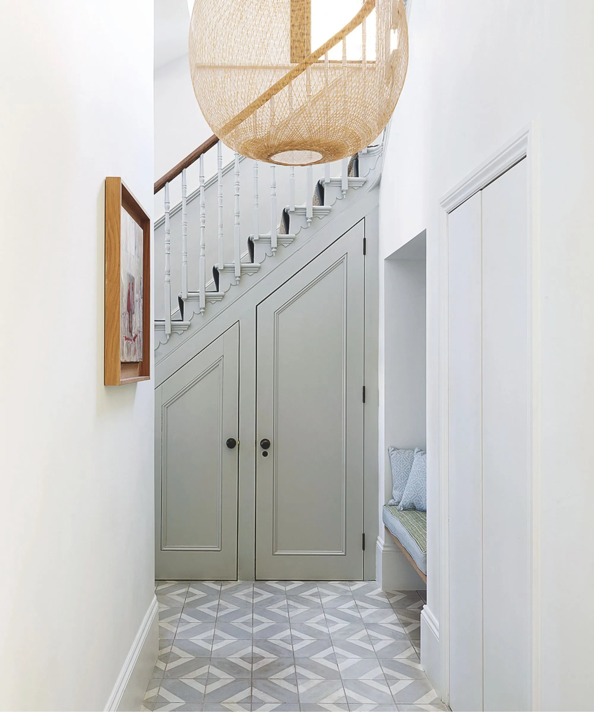 Escalier en pente peint gris avec broches traditionnelles et placards de shaker en dessous avec un grand plafond en osier tissé et des carreaux de sol géométrique' loading='lazy' title=