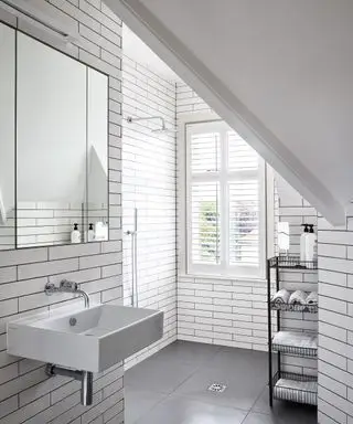 Uma sala úmida com azulejos brancos de metrô com reboco preto e teto inclinado, box para chuveiro
