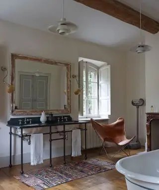 Banheiro neutro, piso de madeira, balcão de lavatório duplo vintage, tapete no chão, cadeira borboleta de couro