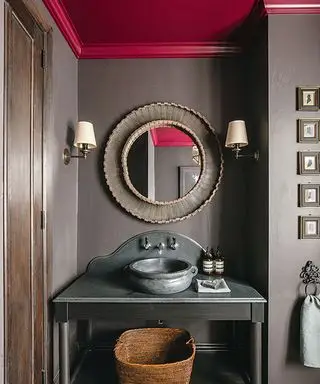Banheiro com paredes e móvel em cinza escuro, espelho redondo e teto decorado em cor ameixa.